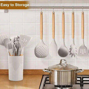 A 12-piece beige kitchenware set with various kitchen tools is on the kitchen table, and food is being cooked.
