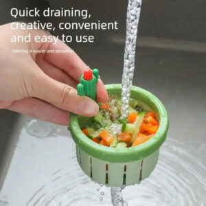 One hand is holding a green cactus-shaped sink strainer filled with leftover food, and is filling the sink with water